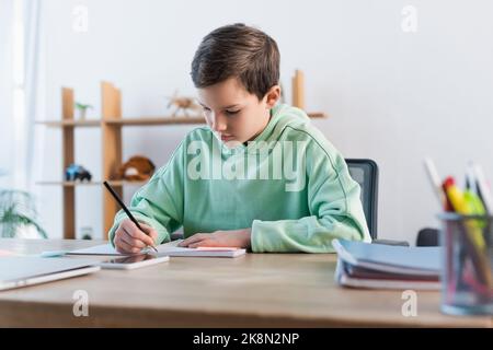 focused boy doing homework and writing in copybook near blurred mobile phone,stock image Stock Photo