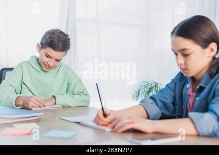 preteen kids writing in notebooks while doing homework on blurred foreground,stock image Stock Photo