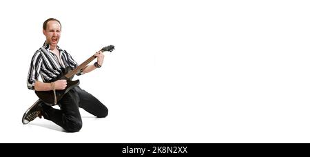 Portrait of young emotive man in stylish clothes playing guitar, posing isolated over white background. Rock musician Stock Photo