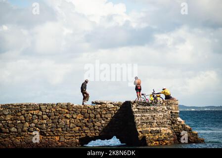 Salvador, Bahia, Brazil - June 04, 2022: People walk on top of the stone breakwater of Porto da Barra beach in Salvador, Bahia. Stock Photo