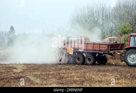 Tractor use manure much spreader trailer to scatter hot steaming horse manure on agriculture field in autumn for natural fertilizer. Stock Photo