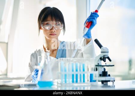 Female scientist making microbiology research using pipette, flask and test tubes working in modern chemical lab. Medicine, biotechnology concept Stock Photo