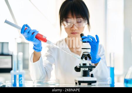 Female scientist making microbiology research using pipette, flask and test tubes working in modern chemical lab. Medicine, biotechnology concept Stock Photo