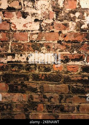 A vertical shot of an old brown and black brick wall with worn spots - grungy brick wall background Stock Photo