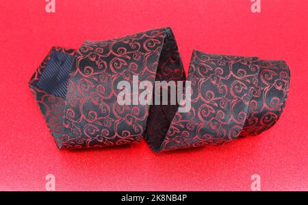 A closeup of an elegant black and red necktie with a floral pattern rolled up on a red background Stock Photo