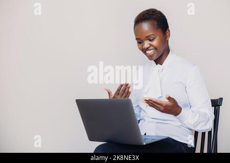 Portrait of attractive cheerful satisfied african woman sitting in chair watching webinar, working online on laptop, talking in video chat isolated Stock Photo
