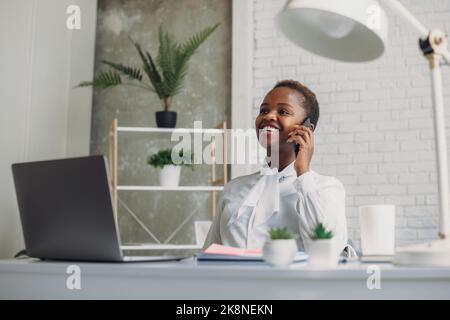African American executive manager accountant using computer while talking on phone in office. Communication with suppliers. Millennial businesswoman Stock Photo