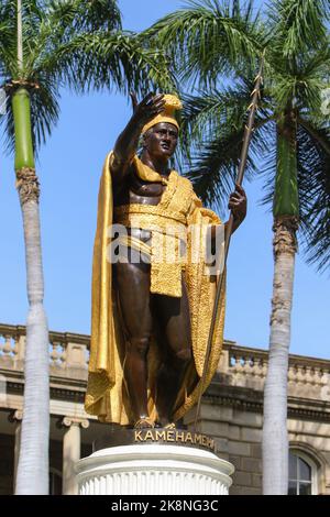 A low-angle vertical of King Kamehameha statue in downtown Honolulu, with palm trees and clear sky background Stock Photo