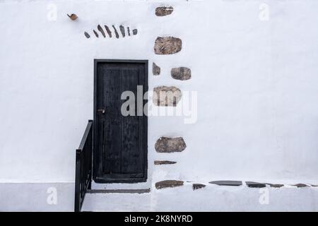 Rustic black wooden door in weathered white wall Stock Photo