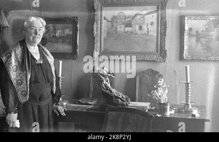 193801: Mrs. Alexandra Thaulow Heggeli. (1862-1955) Artist, worked significantly with leather. She was the sister of Oda Krohg, and married to Frits Thaulow. Here photographed with paintings in the background, possibly Thaulow pictures. Photo: NTB (The glass plate is damaged) Stock Photo