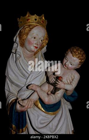 The Christ Child, with golden curly hair, clutches a dove as the Virgin Mary, wearing a jewelled crown, holds him in her arms.  Faithful copy of early 1400s lime wood statue, by an unknown sculptor, in the Roman Catholic St Nikolaus-Kirche at Kaub am Rhein, Rheinland-Pfalz, Germany. Stock Photo