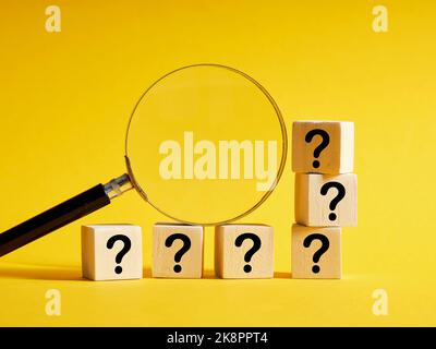 Question analysis, problem solving, research. FAQs, search for an answer, solving a mystery. Magnifying glass with wooden cubes with question marks. Stock Photo