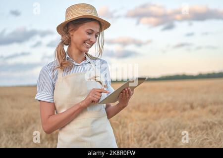 Woman farmer straw hat smart farming standing farmland smiling using digital tablet Female agronomist specialist research monitoring analysis data agribusiness Caucasian worker agricultural field Stock Photo