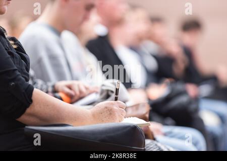 Female hands holding pen and notebook, making notes at conference lecture. Event participants in conference hall. Stock Photo