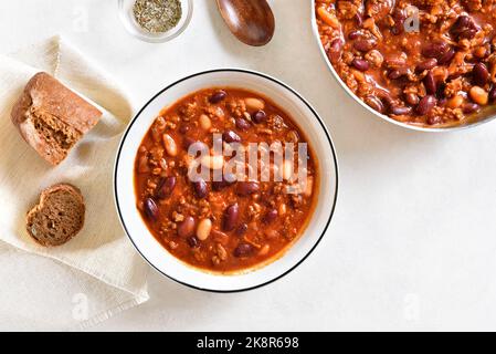Cooked beans with ground beef, jalapeno pepper and bacon in bowl over white stone background. Top view, flat lay Stock Photo