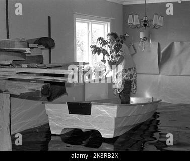 Lillestrøm 19670605 Flood put large parts of Lillestrøm underwater. More than 15,000 people were injured after the flood. Here, a woman has used a small rowboat to evacuate potted plants and more of value from the home where the water reaches her knees inside the living room. Photo: NTB / NTB Stock Photo