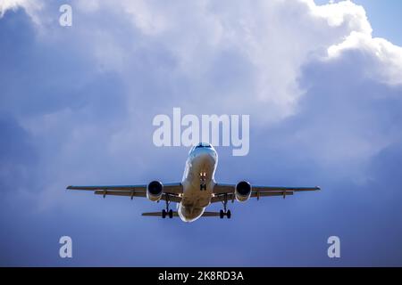 A big white airplane flying in the blue sky with many white and dark blue clouds Stock Photo