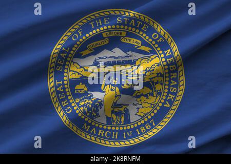 Nebraska US state flag with big folds waving close up under the studio light indoors. The official symbols and colors in fabric banner Stock Photo