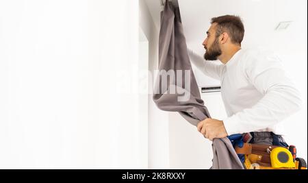 Young man installing curtains over window Stock Photo