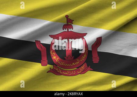 Brunei Darussalam flag with big folds waving close up under the studio light indoors. The official symbols and colors in fabric banner Stock Photo