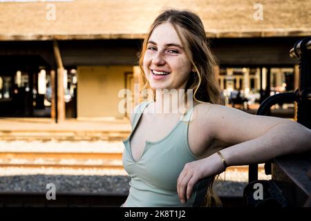 Teenage Girl in Trainyard Standing in Front of Old Black Steam Engine Stock Photo