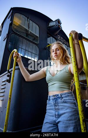 Young Woman Standing on the Stairs of a Diesel Electric Train Engine Stock Photo