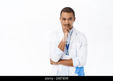 Image of doctor listening with bored face to patient, staring unamused at camera, standing over white background Stock Photo