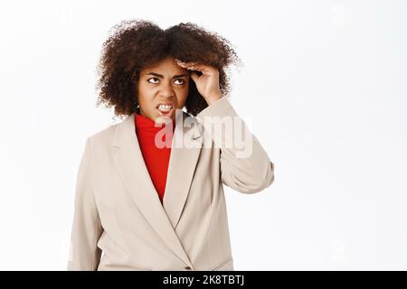 Annoyed and tired african american businesswoman, bothered with work, touches head feels headache and stress, stands over white background Stock Photo
