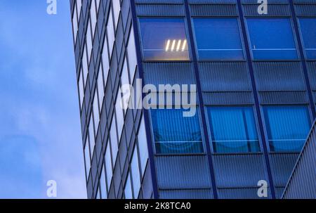 Office windows at dusk, anonymous corporate façade, solitude, isolation and urban alienation in contemporary city life. Only one room lighted. Stock Photo