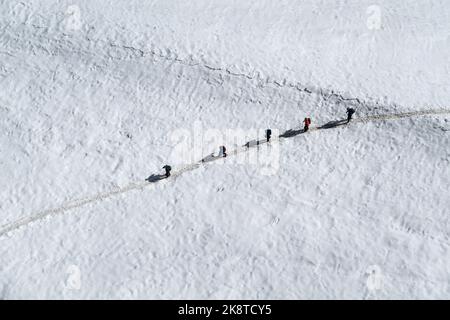 Chamonix, France - 31 August, 2022: View from above of 5 walkers secured together with ropes walking across the Valle Blanche glacier in summer Stock Photo