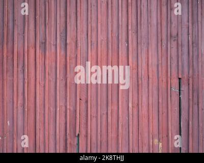 Red wooden planks background. Partially broken and weathered boards. Texture of a building exterior of an old house. A vertical design pattern. Stock Photo