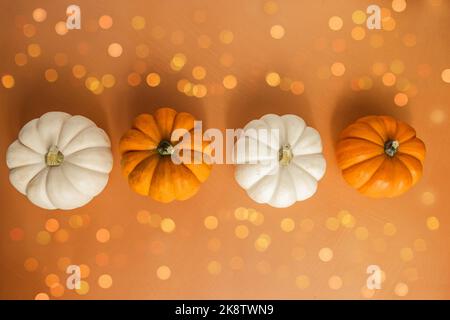 A line of miniature pumpkins and leaves on a neutral orange surface for harvest Halloween October November home decor Stock Photo