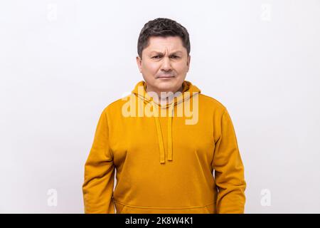 Portrait of sad upset dark haired man standing and looking at camera with dissatisfied sadness face, expressing sorrow, wearing urban style hoodie. Indoor studio shot isolated on white background. Stock Photo