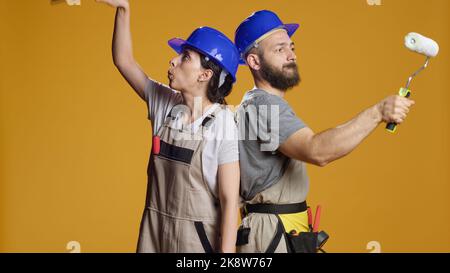 Team of builders with refurbishment skills painting walls with paintbrush and roller, using brush and color to renovate. Constructors working on redevelopment and building in studio. Stock Photo