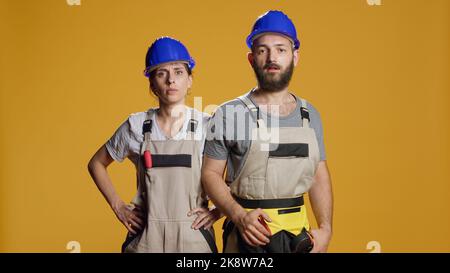 Happy constructors dancing and singing in studio, having overalls and helmets. Doing dance moves and having fun before working on construction site, funny mechanics enjoying music. Stock Photo