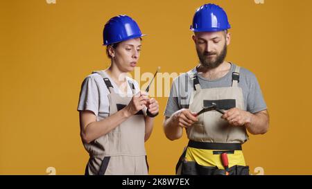 Man and woman builders using screwdriver and wrench to work on construction and industrial rebulding. Team of contractors working with repair tools, holding turnscrew and spanner in studio. Stock Photo