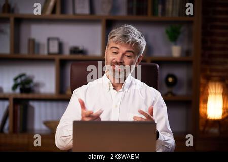 Successful man talking over laptop webcam in virtual chat sitting at workplace. Businessman in glasses, having online conversation conducting business Stock Photo