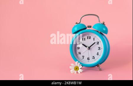 Blue alarm clock with a daisy on pink background, banner with copy space for text. Time management, planning, healthy sleep habits, reserve your time, book appointment concept feminine style. Stock Photo