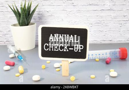 Annual Check-up text on paper with heart beat diagram, stethoscope, delicious green apple, measurement tape and blue dumbbell on wooden table - medica Stock Photo