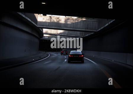 Black car is driving down the road in the tunnel. Traffic infrastructure, tunnel architecture, light effect. Stock Photo