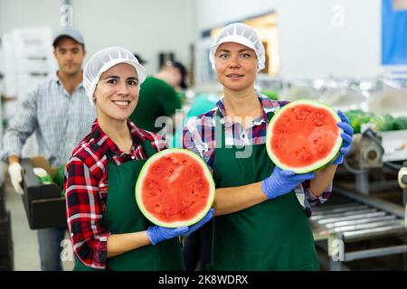 Portrait of two happy smiling factory workers holding halves of ripe red watermelons in hands Stock Photo