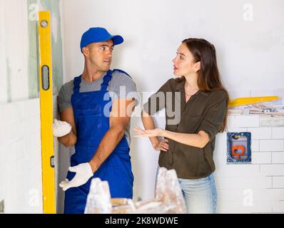 Worker using spirit level on wall with woman client Stock Photo