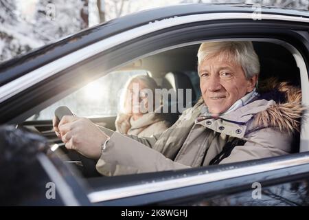 Portrait of cheerful senior couple driving car in winter, focus on senior man behind wheel looking at camera, copy space Stock Photo