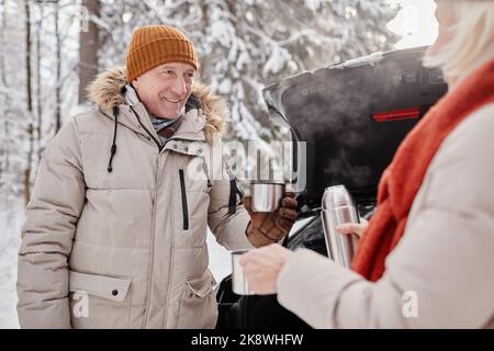 Waist up portrait of happy mature couple enjoying cup of hot coco outdoors during winter hike Stock Photo