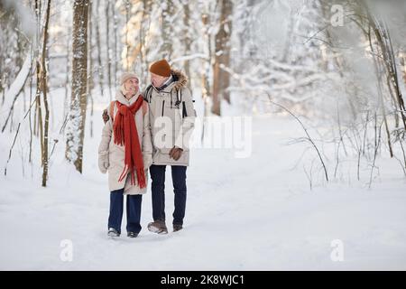 Full length portrait of happy senior couple enjoying walk in winter forest and looking at each other, copy space Stock Photo