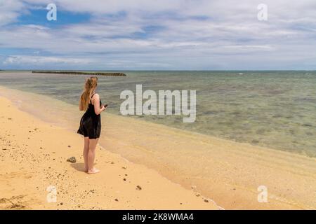 Woman standing on isolated beach in Hawaii wearing a black dress. Stock Photo