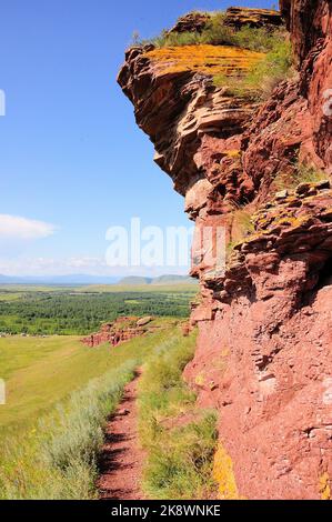 A narrow path going up the hillside along a red and high stone formation. Mountain range Chests, Khakassia, Siberia, Russia. Stock Photo