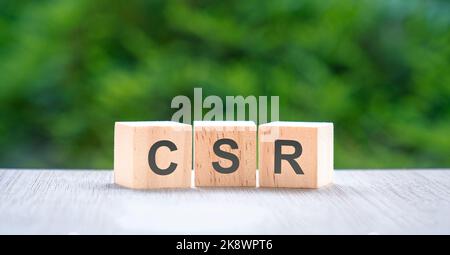 CSR, letters on wood block cube with green nature background. Corporate social responsibility concept. Stock Photo