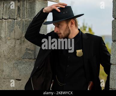 Sheriff or cowboy in black suit and cowboy hat. Man with west vintage pistol revolver gun. American western, sheriff. Stock Photo