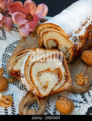Homemade plum and walnut strudel noodles decorated with powdered sugar on a wooden base with a rose. Conceptual banner for gastronomy. Stock Photo